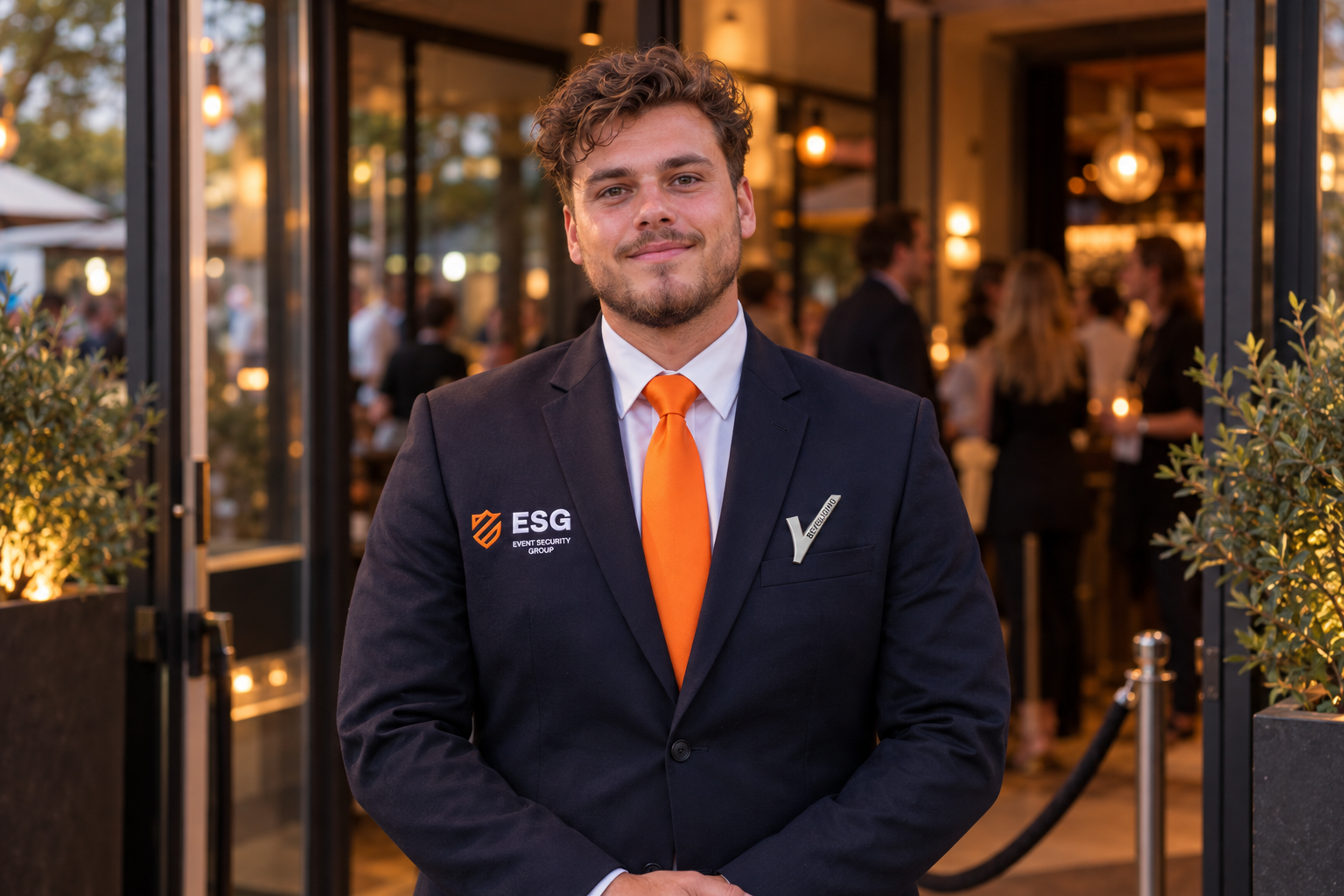 Een gastvrije ontvangst bij de deur, in het donkere ESG-pak met oranje stropdas