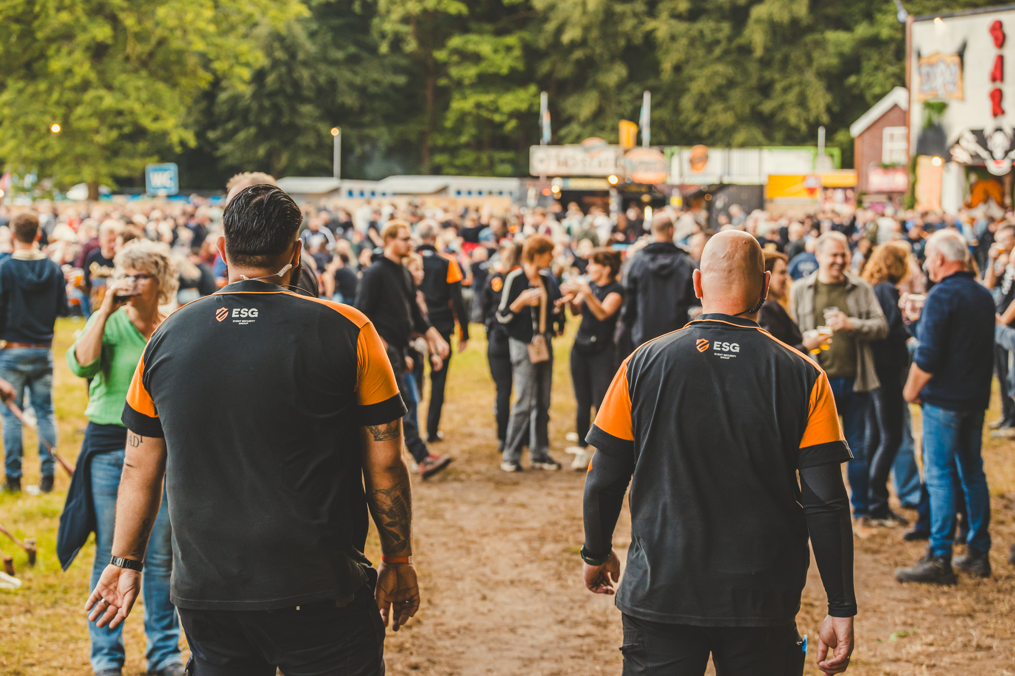 Twee ESG-beveiligers lopen samen over een druk festivalterrein
