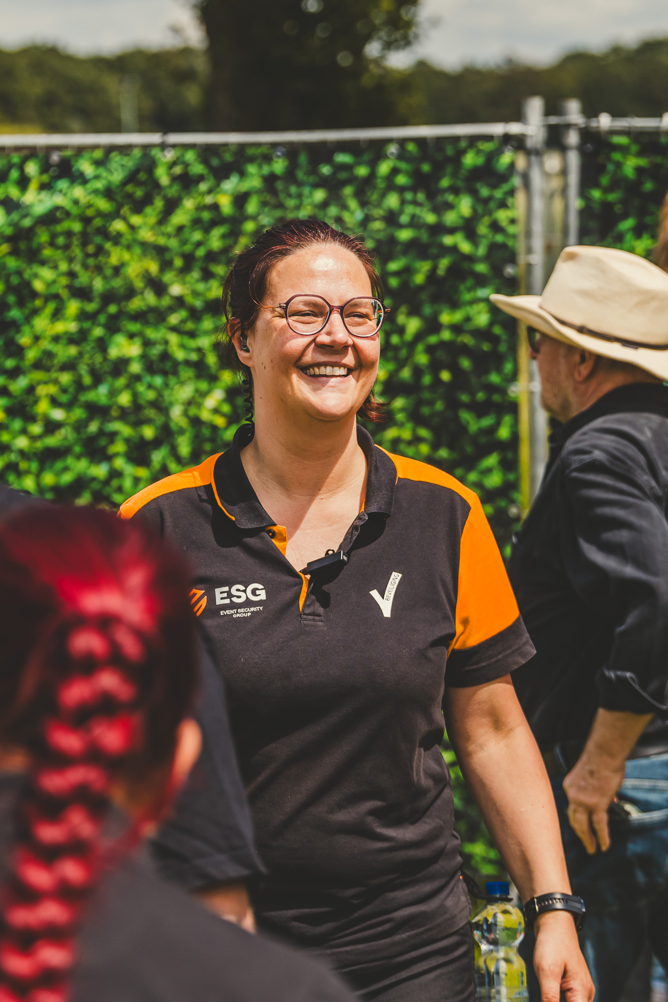 Een lachende ESG-beveiliger in de zwart-oranje polo tussen bezoekers
